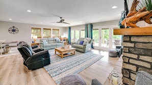 A spacious living room with a fireplace, a ceiling fan, and a large window with curtains.
