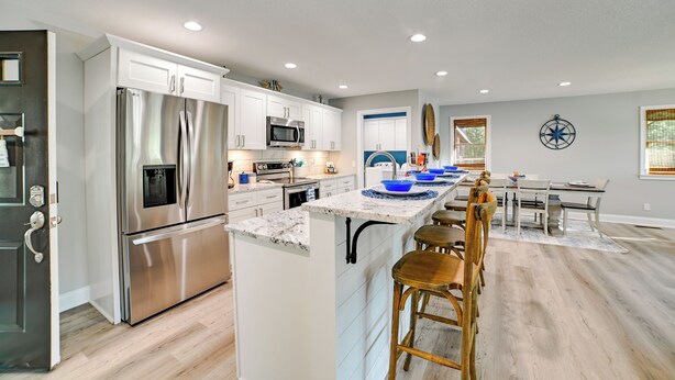 A modern kitchen with stainless steel appliances, a central island with bar stools, and a dining area with a table and chairs.