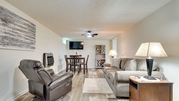 A living room with a leather recliner, a sofa, a wooden side table, and a TV mounted on the wall. - Pet-friendly Zanesville Haven w/ Game Room! (Zanesville)