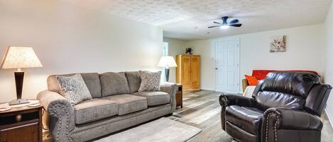 A living room with a brown leather sofa, a brown leather recliner, a wooden side table, a lamp, and a wooden floor.