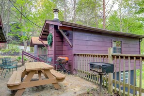 Une cabane en bois avec une table de pique-nique et un espace barbecue, entourée d’une clôture en bois et d’arbres.