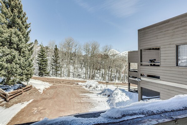 A modern building with a wooden exterior, a dirt road, snow-covered ground, and a forest in the background. - Cozy La Veta Condo: Walk to Cuchara Mountain Park! (La Veta)
