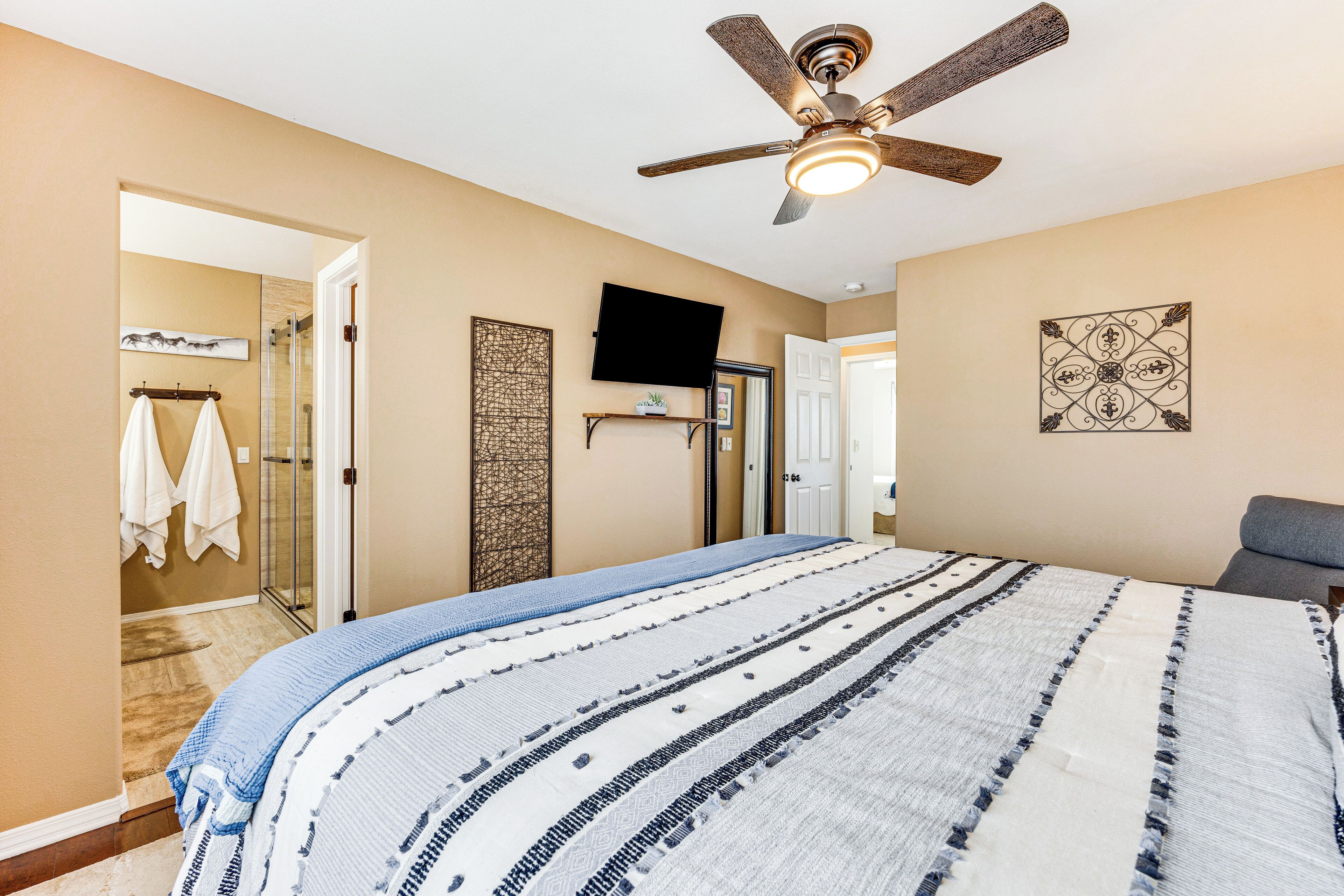 A bedroom with a bed, a ceiling fan, a TV, and a door leading to a bathroom.