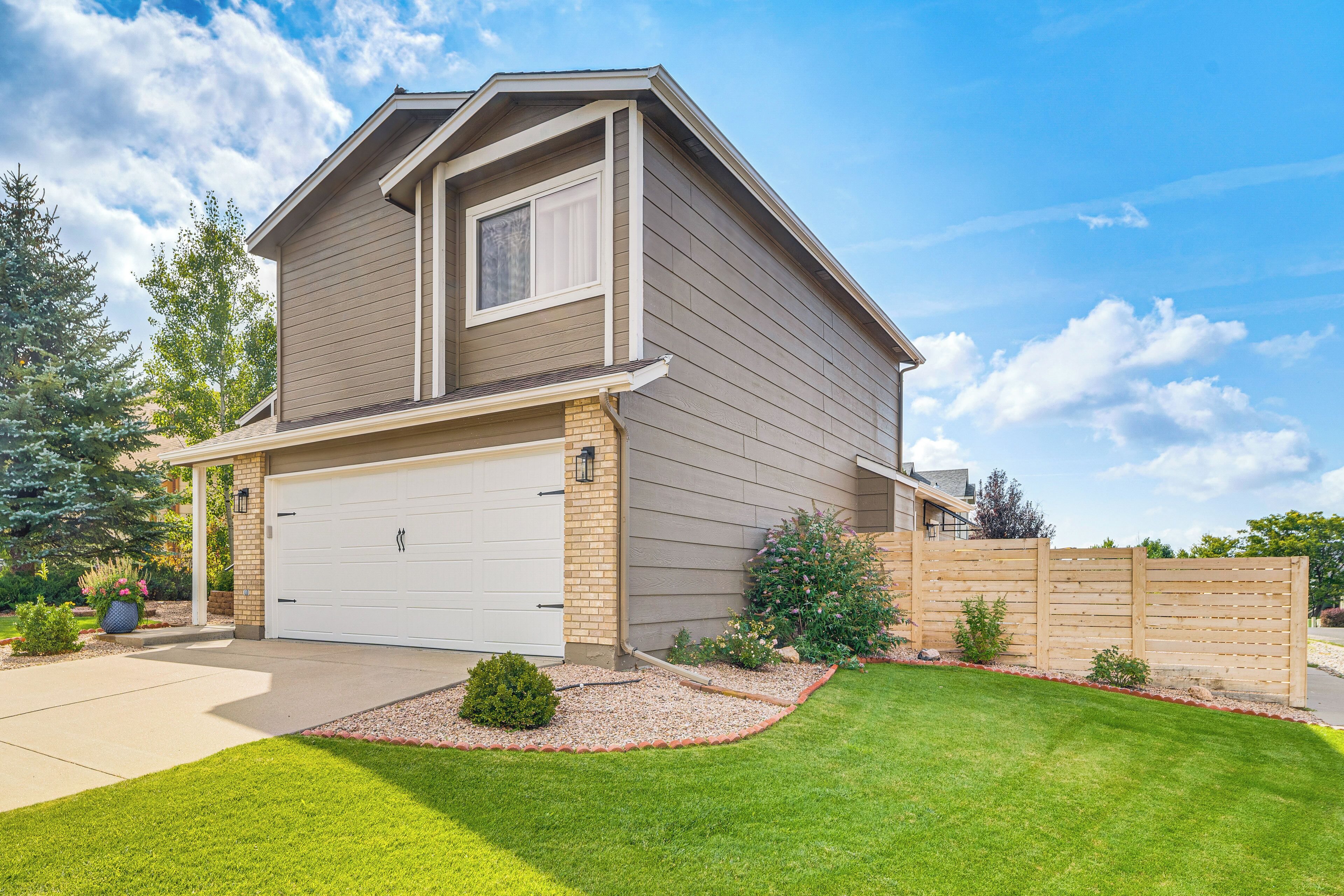 A two-story house with a garage, a well-maintained lawn, and a wooden fence.