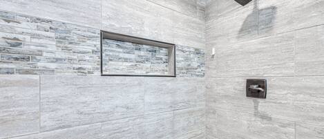 Zona de ducha con pared de azulejos, un cuadro enmarco y panel de control de la ducha.