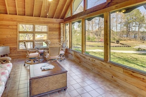 A wooden cabin interior with a dining area, wicker furniture, and large windows offering a view of the outdoors. - Lakefront Leesburg Home w/ Private Dock & Ramp! (Leesburg)