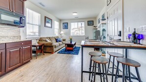 Un vaste espace de vie comprenant une cuisine, un plancher en bois, un canapé, une table basse et un bar avec des tabourets.