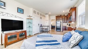 Un salon spacieux doté d’un grand téléviseur à écran plat, d’un meuble de rangement en bois et d’un lit confortable avec une literie bleue et blanche.