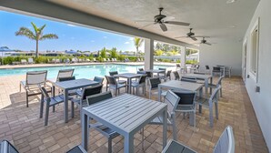 Un espace extérieur avec piscine, comprenant des chaises longues et des tables, des ventilateurs de plafond, et offrant une vue sur la piscine et les environs.