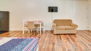A living room with a beige sofa, a dining table with chairs, a flat-screen TV mounted on the wall, and a patterned rug on the floor. - ATV Trail Access: Mountain-view Briceville Studio! (Briceville)