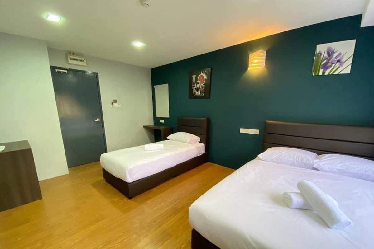 Habitación de hotel con dos camas, piso de madera, una pared de acento verde oscuro y un escritorio pequeño.