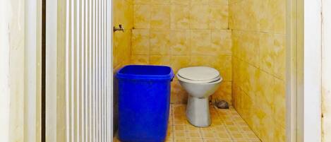 Un baño pequeño con azulejos amarillos estampados, un inodoro blanco y un cubo de basura azul.