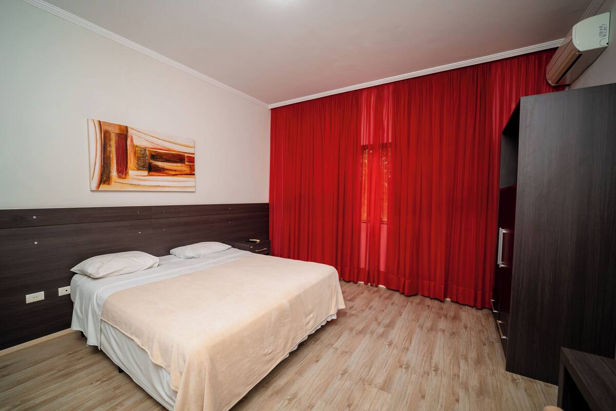 Ein Schlafzimmer mit einem Bett, einem Kopfteil, einem roten Vorhang und einer Wand-Klimaanlage.