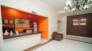 Un área de recepción con mostrador, un cuadro abstracto de gran tamaño, un refrigerador y un sofá marrón.