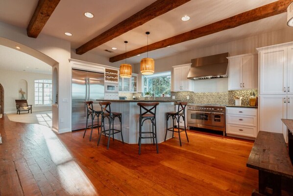 A spacious kitchen with a large island, wooden beams, and modern appliances. - Villa Serena | Pool, Pickleball & Luxury Retreat (Fallbrook)