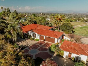 A house with a red-tiled roof, a garage, and a landscaped garden with palm trees. - Villa Serena | Pool, Pickleball & Luxury Retreat (Fallbrook)
