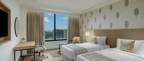 A hotel room with two beds, a desk, a chair, a TV, and a window with a city view.