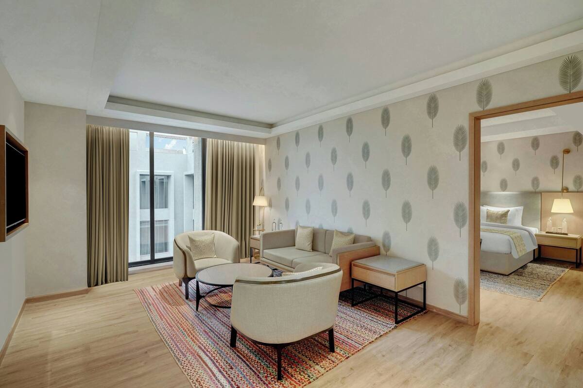 A hotel room with a sofa, armchairs, a small table, a mirror, and a bed with a nightstand.