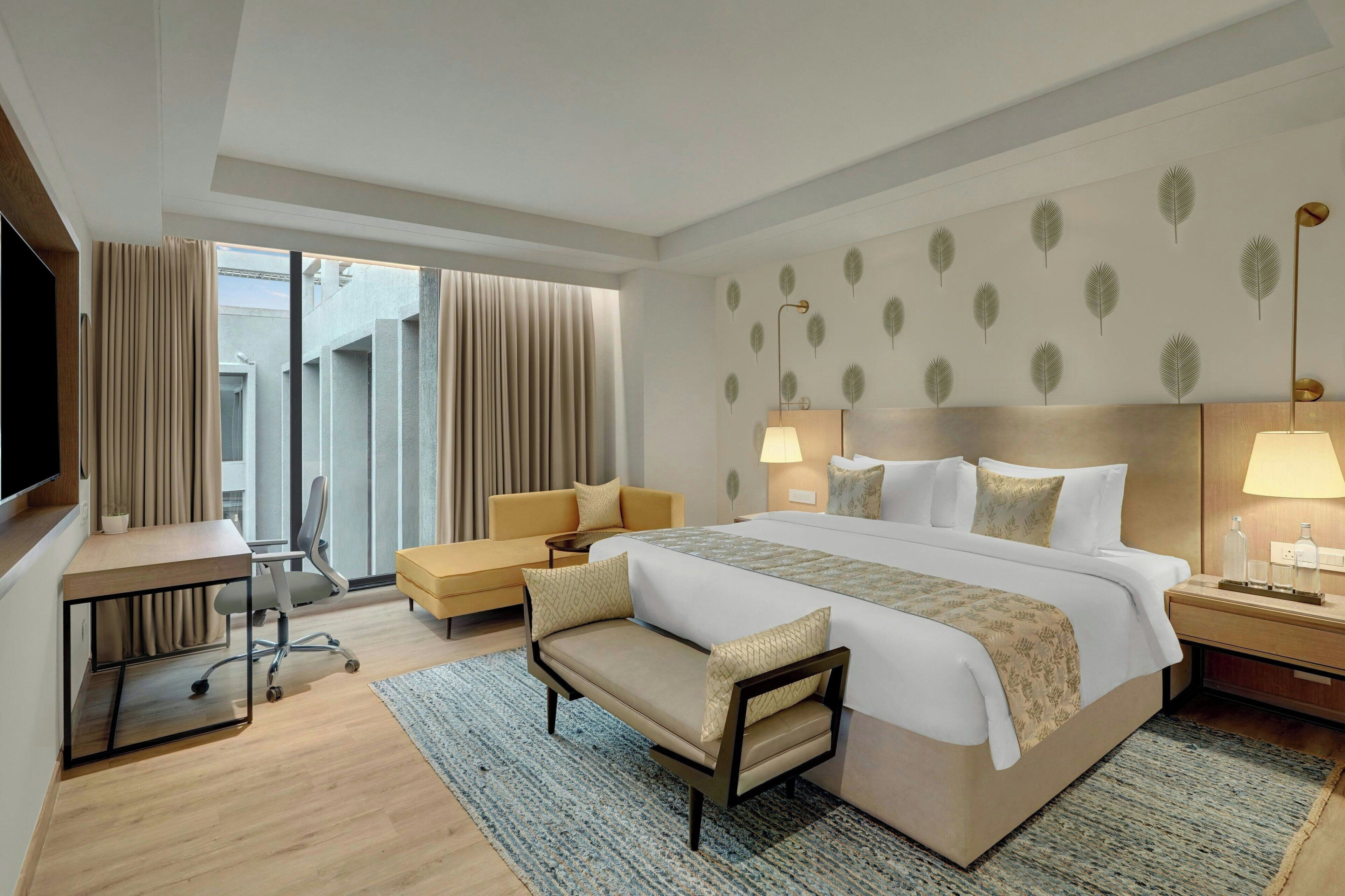 A hotel room with a large bed, a desk, a sofa, and a view of the outdoors.