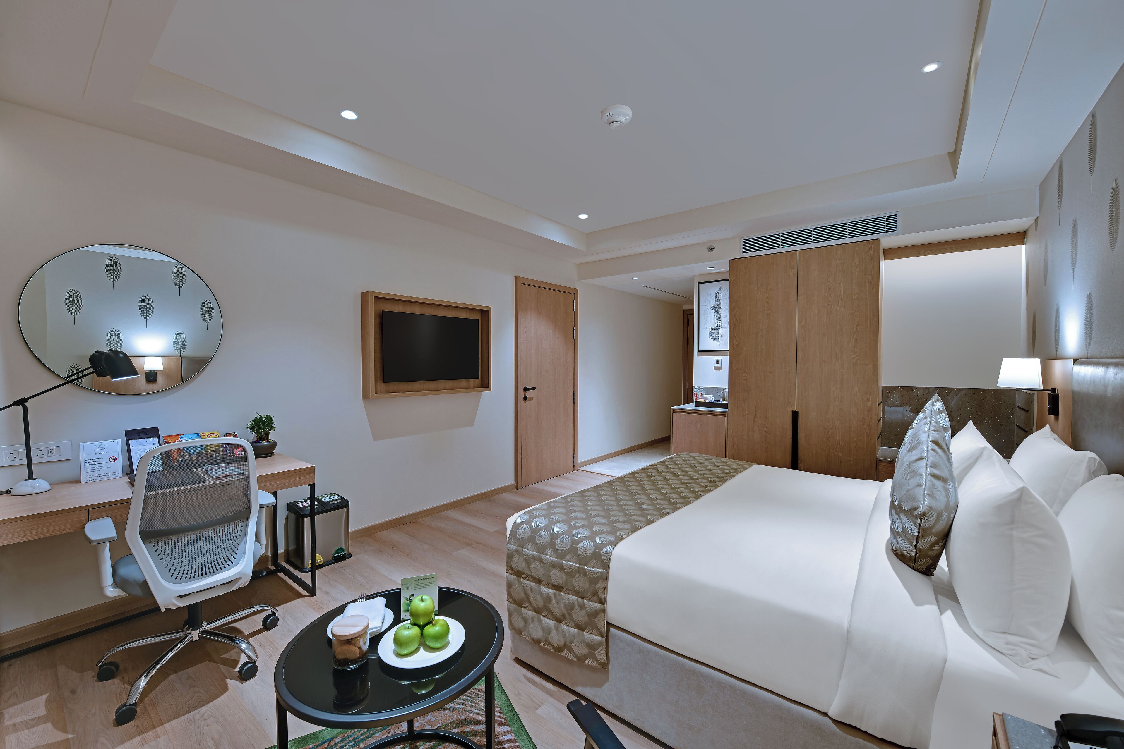 Quarto de hotel com cama, escrivaninha, cadeira e televisão.