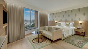 A hotel room with a bed, a sofa, a TV, a nightstand, and a view of the city.