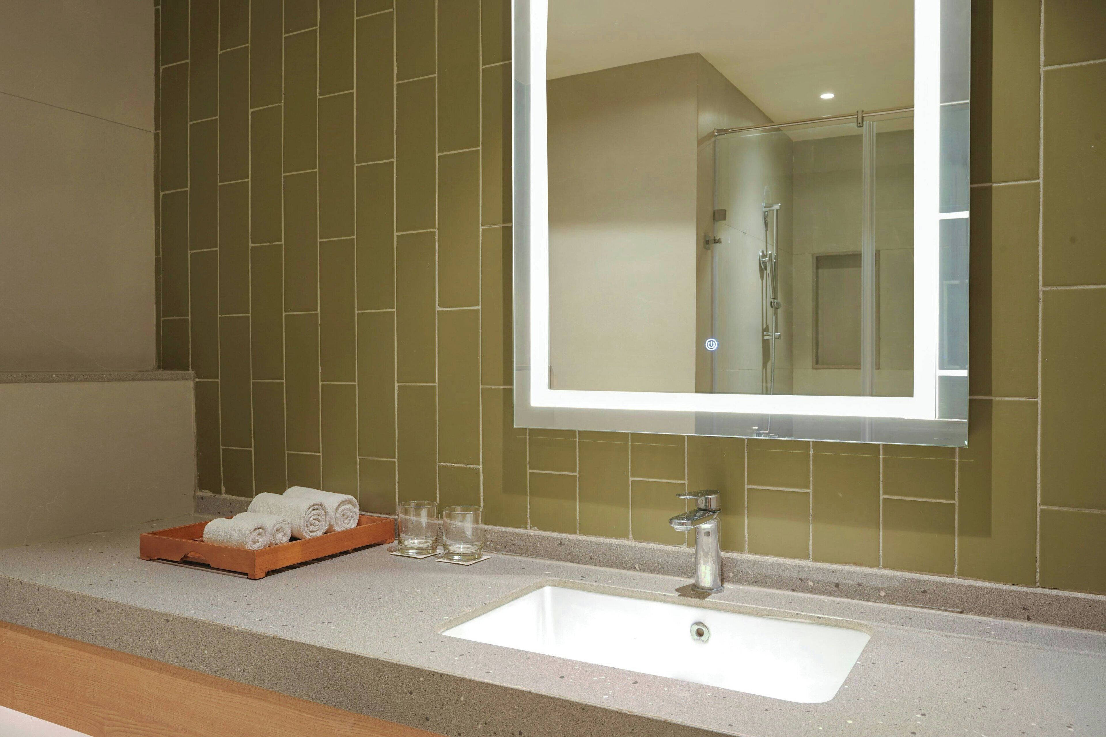 A bathroom with a large mirror, a sink, and a tray with towels and glasses.