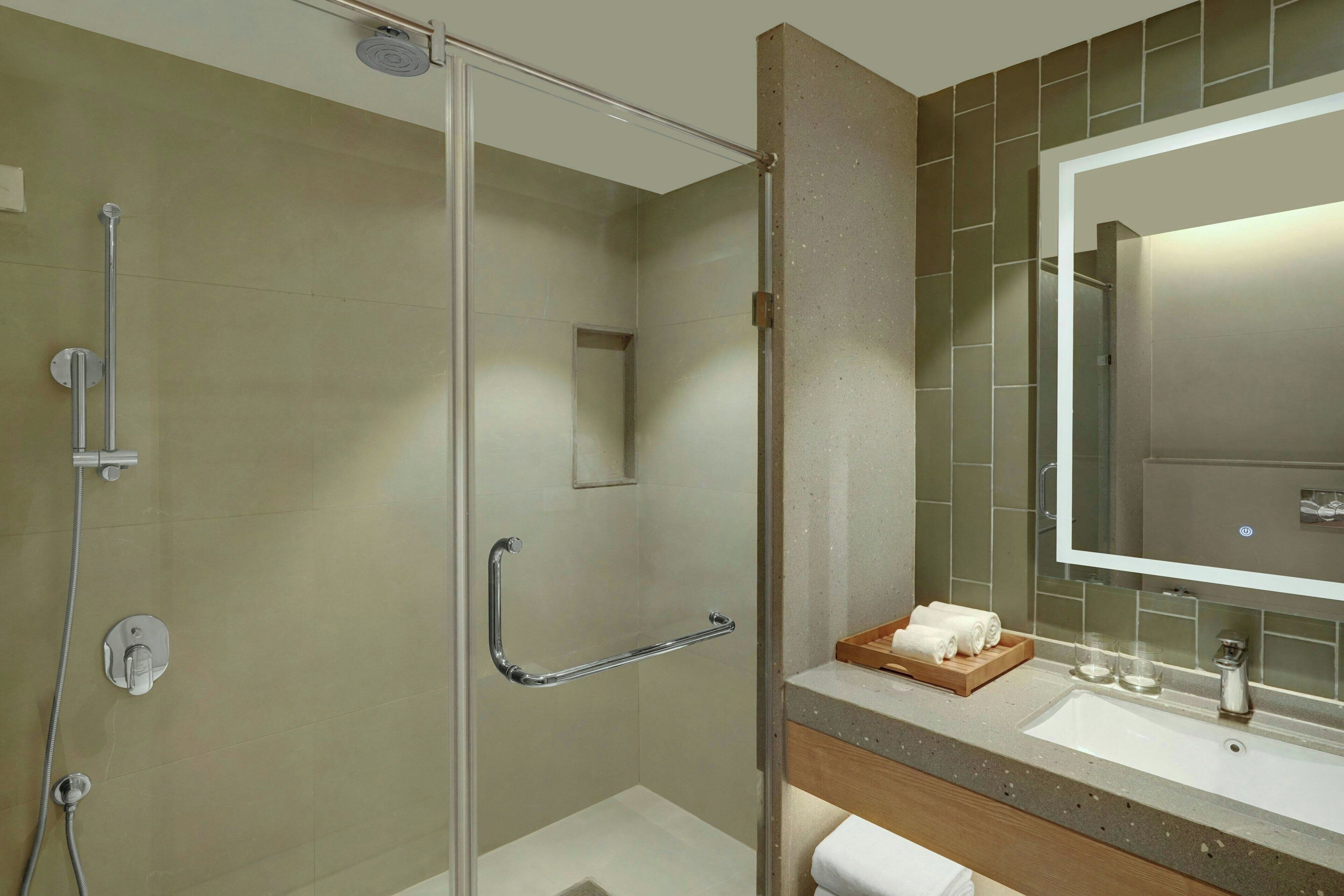 Un baño moderno con ducha de vidrio, tocador con espejo y lavamanos.