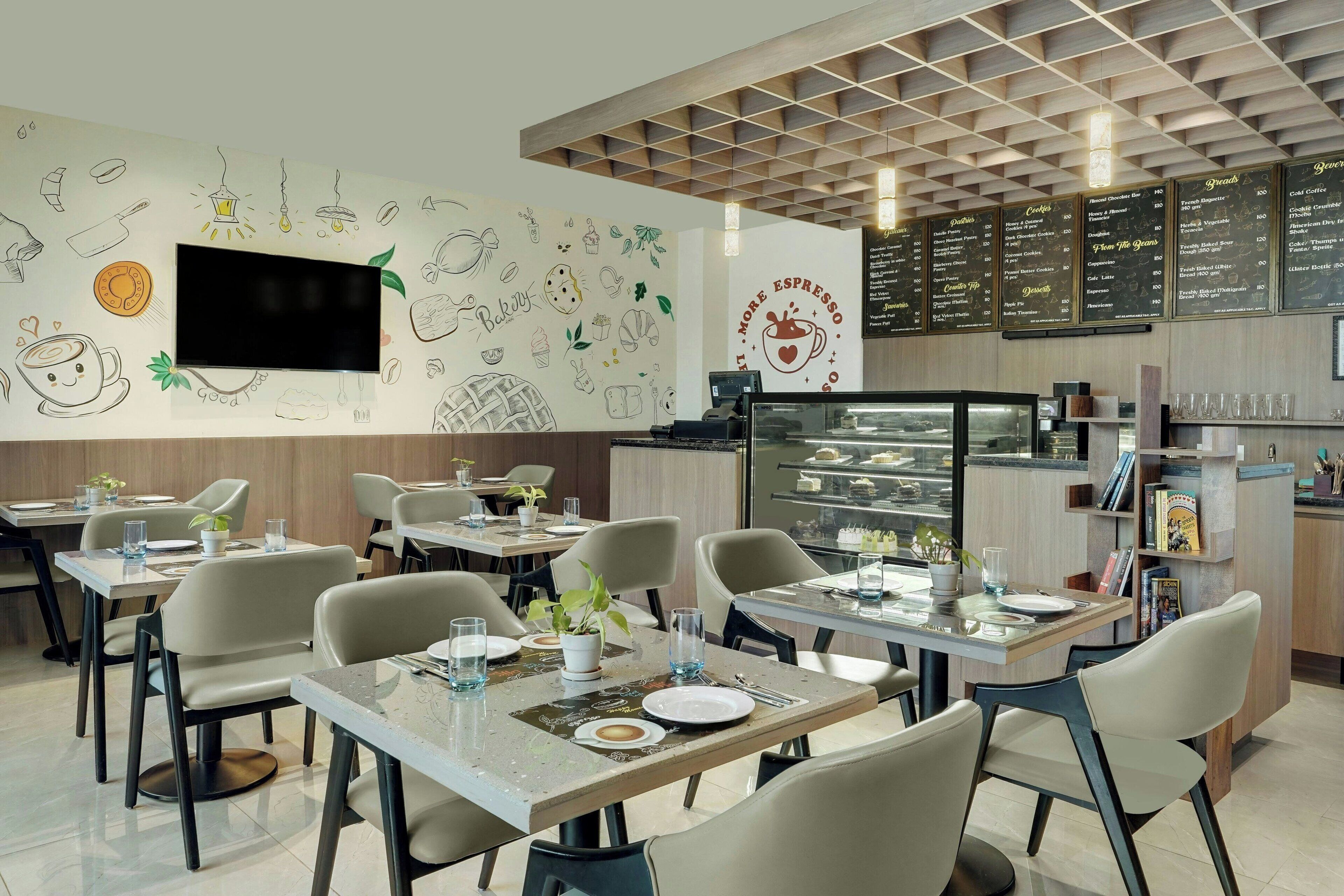 A modern cafe with tables and chairs, a menu board, and a wall with drawings of food and coffee.