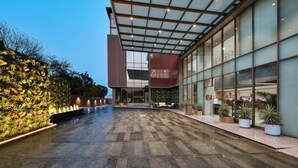A modern building with a glass facade, a covered outdoor area with a tiled floor, and a vertical garden on the left.