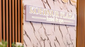 A sign for Kohinur Plaza hotel & spa with a marble wall background.