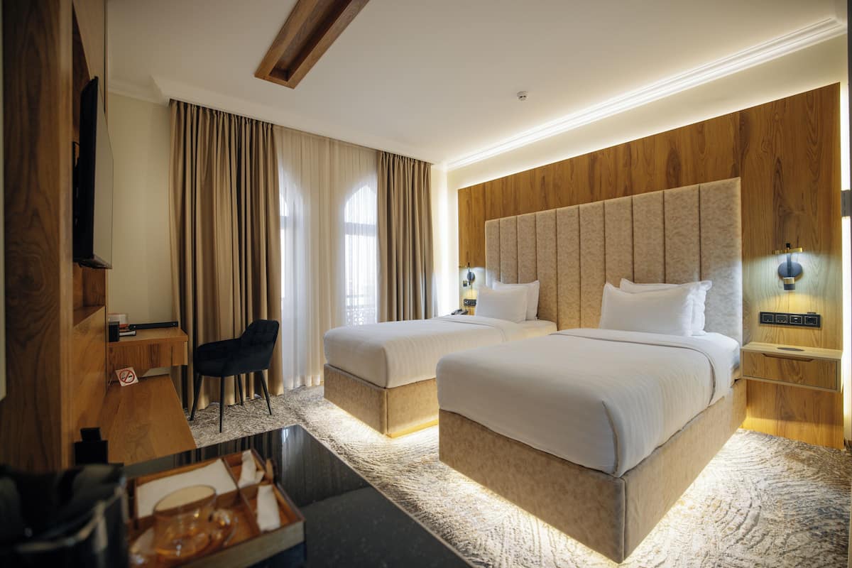 A hotel room with two beds, a desk, a chair, and a TV.