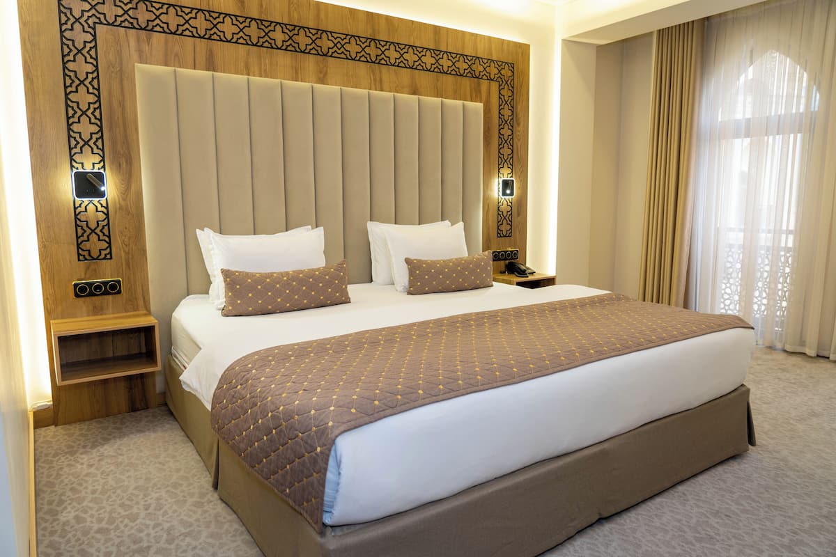 A hotel room with a large bed, a bedside table, a nightstand, and a wall-mounted phone.