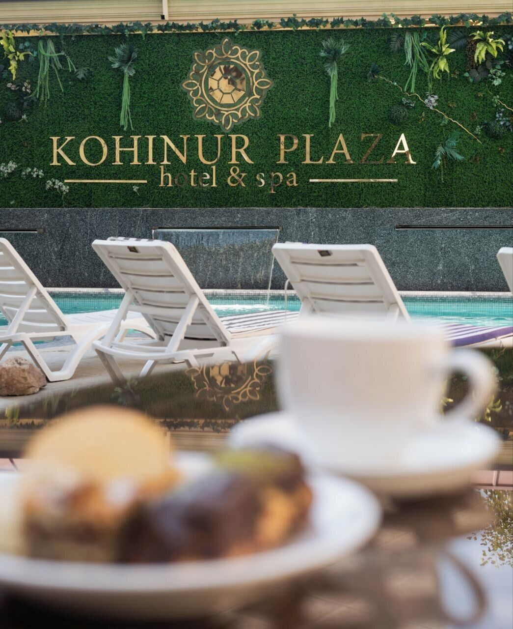 Zona de piscina con sillones de descanso y un cartel del hotel y spa Kohinur Plaza.