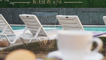 Zona de piscina con sillones de descanso y un cartel del hotel y spa Kohinur Plaza.
