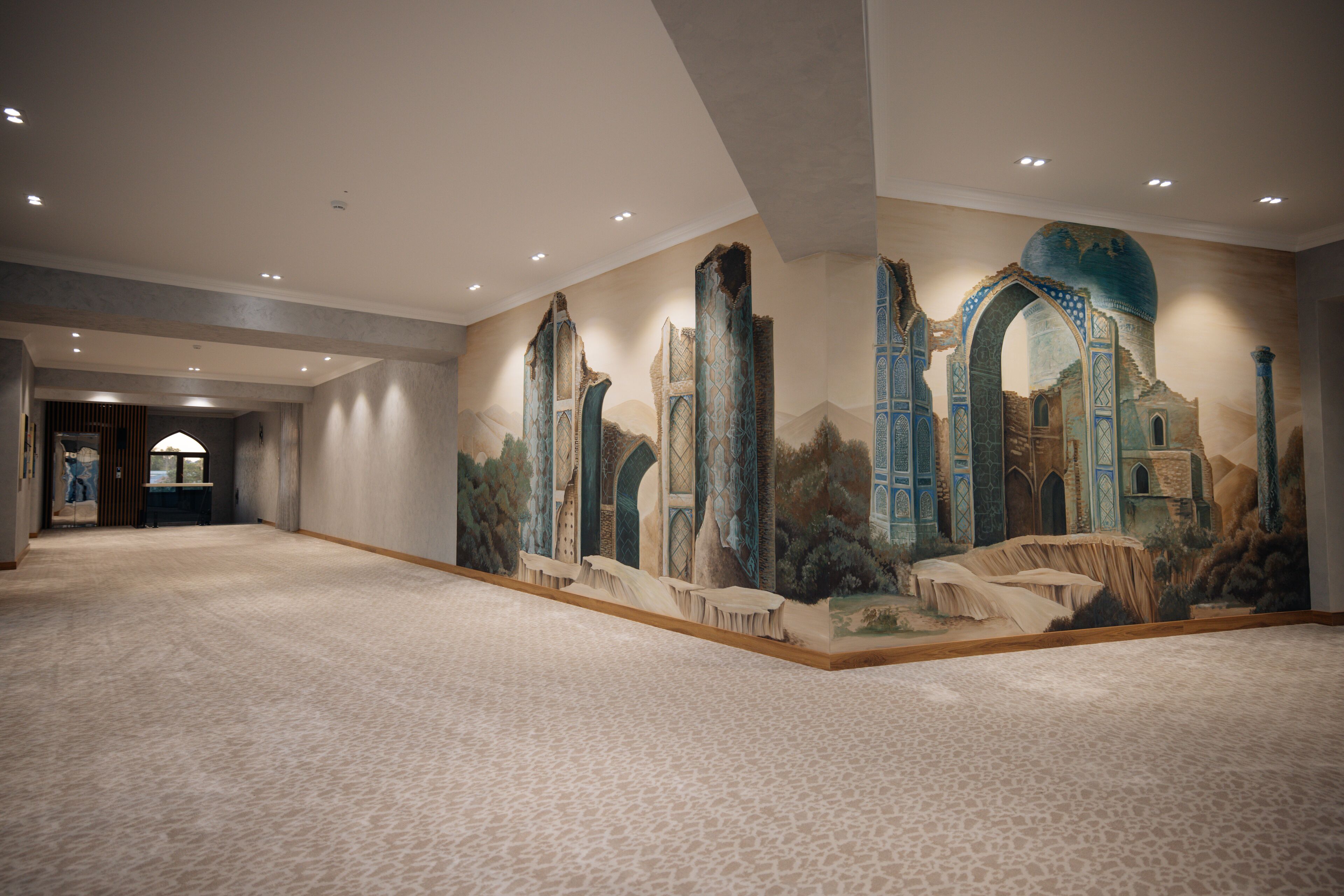 A spacious hotel lobby with a large mural depicting ancient architecture and a carpeted floor.