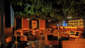 A bar area with orange seating, a bar counter, and a wall with a patterned design. - Kohinur Plaza (Samarkand)