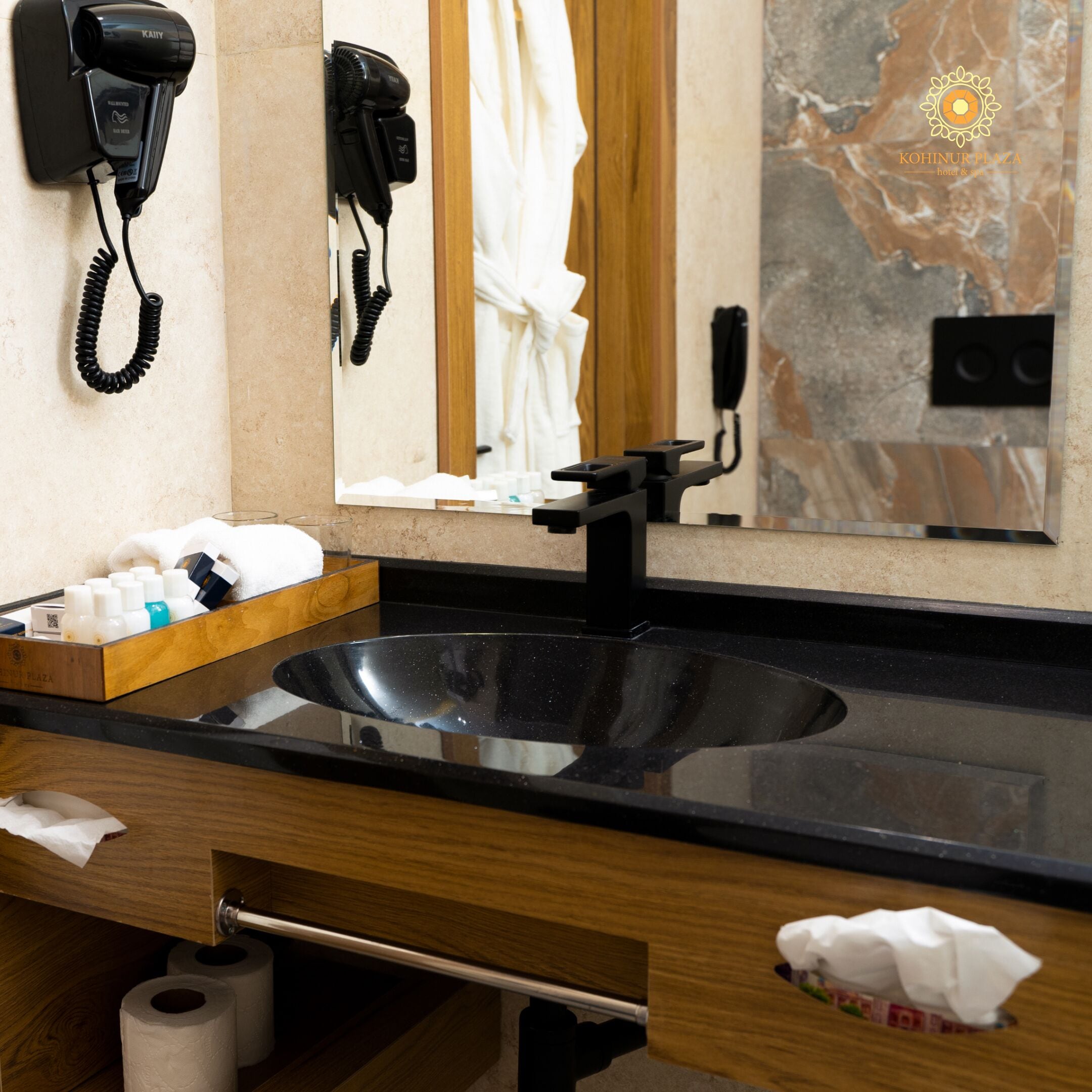 Un baño con un lavabo negro, un mueble de tocador de madera, un espejo y un secador de pelo montado en la pared.