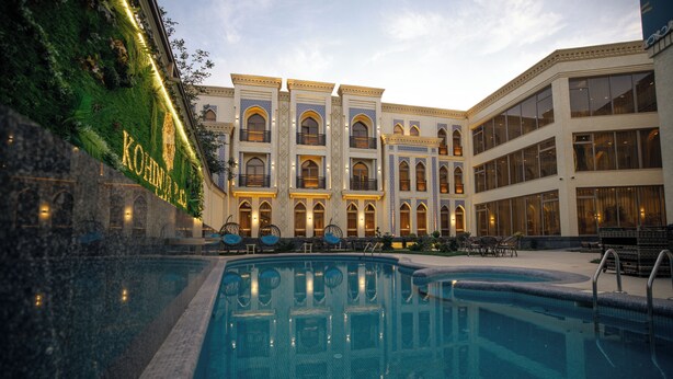 A hotel with a swimming pool, outdoor seating, and a well-lit facade.