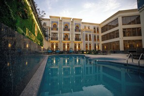 A hotel with a swimming pool, outdoor seating, and a well-lit facade. - Kohinur Plaza (Samarkand)