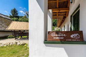 A wooden sign with 'Klemintina Vendeghez' and a house illustration, a thatched roof structure, and a white building with a green window. - Klementina's Guest House (Nemesvita)