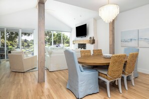 A modern dining area with a round wooden table, light blue upholstered chairs, and a chandelier. - Permanent Waves, Gorgeous home, Golf Course Views! (Isle Of Palms)