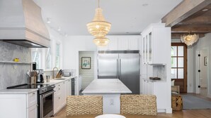 A modern kitchen with white cabinetry, a stainless steel refrigerator, and a wooden dining table.
