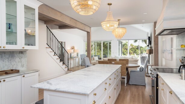A modern kitchen with white cabinetry, a marble island, and a staircase leading to a dining area.