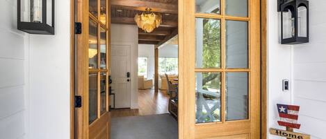 A wooden door with glass panels leading to a room with a ceiling fan and a view of the outdoors.