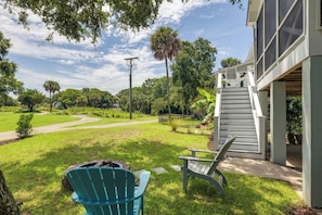 A backyard with a paved path, a fire pit, outdoor furniture, and a staircase leading to a covered area.