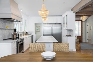 A modern kitchen with a central island, stainless steel appliances, and a hanging chandelier.