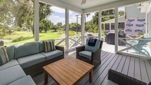 A covered porch with wicker furniture, a wooden table, and a view of a golf course.