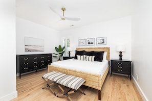 A bedroom with a bed, a bench, a nightstand, a lamp, a ceiling fan, and a wall-mounted picture.