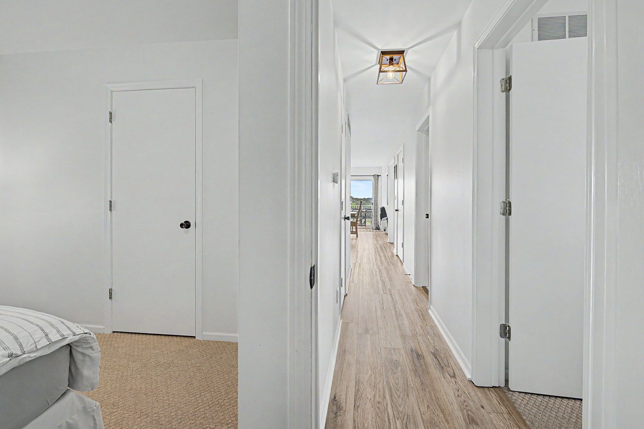 A corridor with white doors, a wooden floor, and a hanging light fixture.