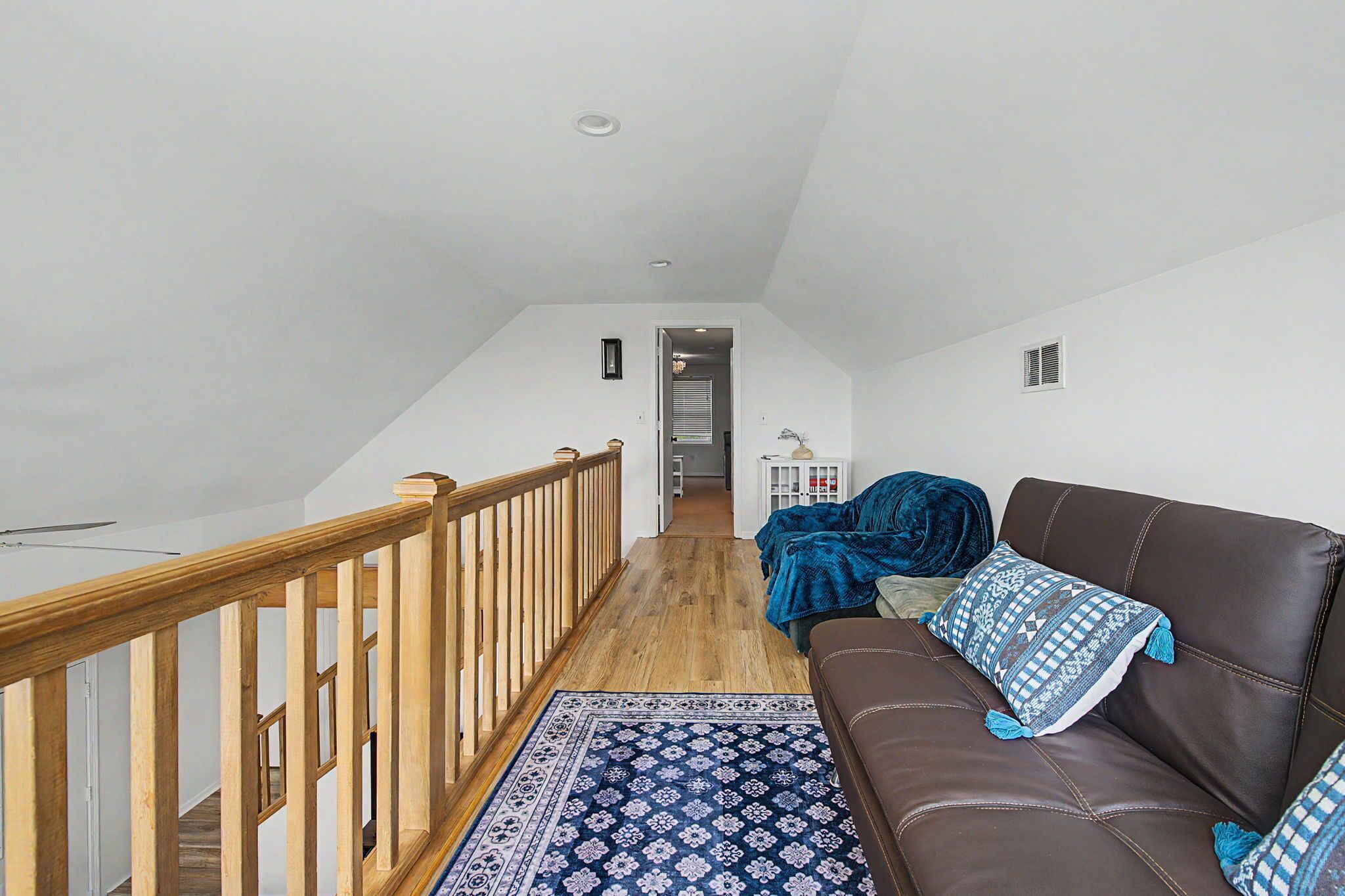 A spacious loft with a wooden staircase, a brown leather sofa, and a patterned rug.